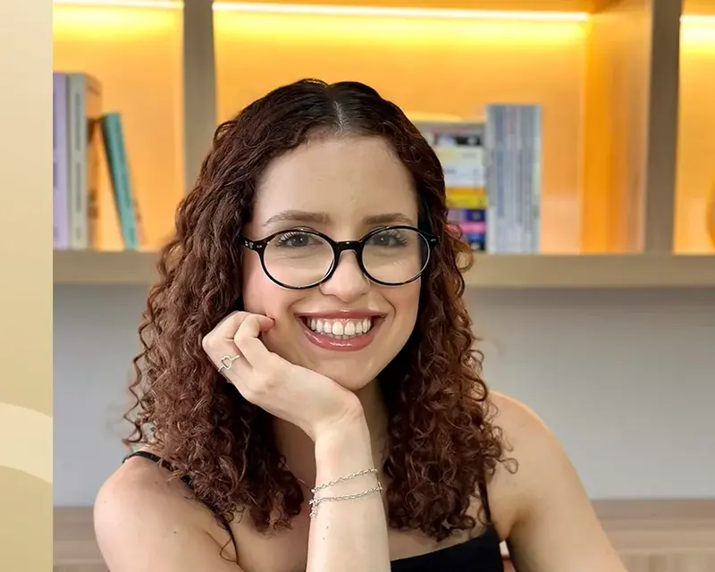 Ana Cláudia, nutricionista, sorrindo de óculos no consultório